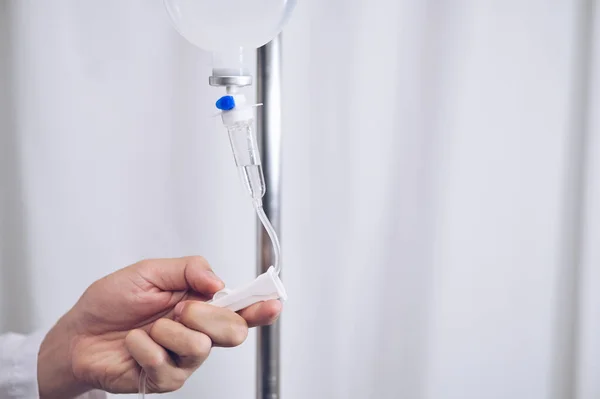 Close up saline IV drip Infusion doctor adjusted volume rate of intravenous fluid bottle with IV solution for patient in ward hospital.