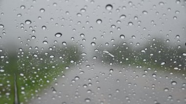 Yolda cam arabanın camına yağmur damlaları düşer.