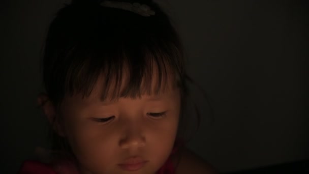Küçük kız tablet içinde video izliyor. Gece vakti ekrandan yansıyan ışık, çocuklar oyun oynuyor. Çizgi film kavramları izliyor. — Stok video
