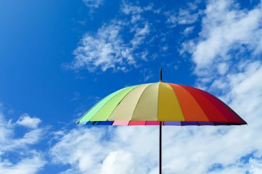 Mavi gökyüzü bulutu arka planında çok renkli bir şemsiye