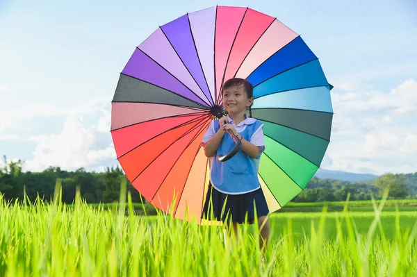 Little girl under colorful umbrella in rice field scene — Stock Photo, Image