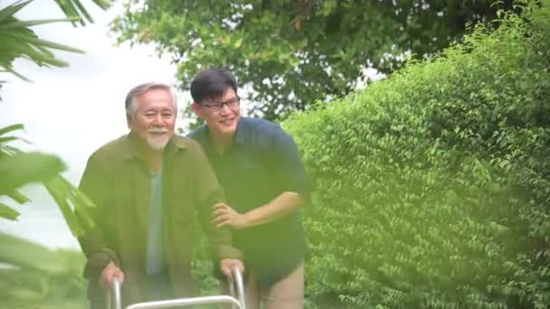 Zoon helpen verzorger oude vader met het lopen op pad weg naar huis tuin voor relaxant of revalidatie fysiotherapie — Stockvideo