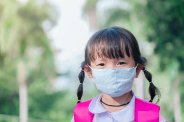 Küçük okul kızının maskesi var. Çocuk okula gittiğinde kendini Coronavirus COVID-19 'dan koruyor. Burnunda hastalık ya da hava kirliliğinden korunmak için maske takan bir öğrenci.