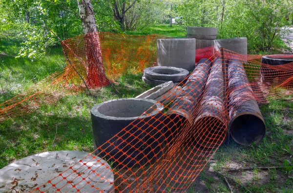 Steel pipes and concrete rings of various sizes used on the construction site of a water pipe in a residential area