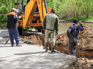 Bir kazıcı ve üç kazıcı birikmiş yağmur suyunu boşaltmak için bir kanalizasyon borusu açmak için bir çukur kazıyor. Güneşli yaz günü.