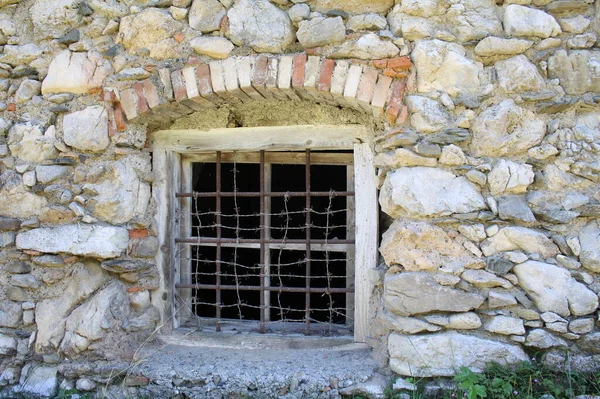 Window with railing in an old stone wall, dark interior, brick arch.