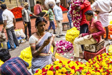 Bangalore, Karnataka, Hindistan 'daki renkli KR çiçek pazarında kalabalık bir günde müzik dinleyen kadın çiçekçi. Fotoğraf 3 Mart 2018 'de çekildi..