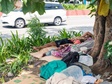 Manila, Filipinler - Haziran 2020: Çocuğuyla birlikte evsiz bir adam, cadde boyunca bir ağacın yanındaki kartondan yapılmış derme çatma bir yatakta uyur..