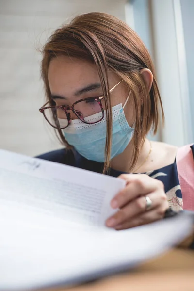 外科用マスクをしたアジア系女性が契約書をレビューする 新常態概念 — ストック写真