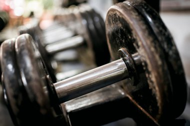 Bir dambıl sapına yakın çekim. Spor salonundaki rafta duran bir sıra dambılın arkaplan görüntüsü.