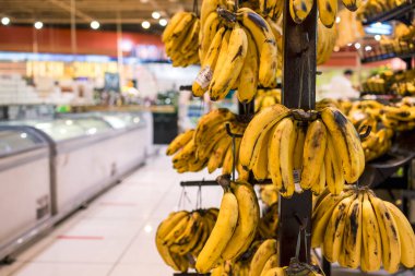 Yakın çekim olgun muzlar süpermarketin meyve reyonunda kancalarla ahşap bir direkte asılı duruyor..