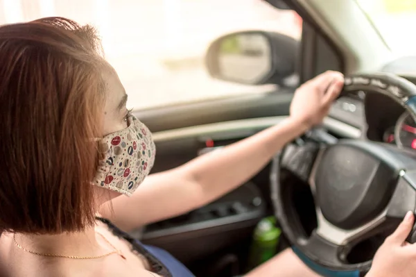 フェイスマスクと夏服を着たアジア系の女性が小さな車を運転する 車内の俯瞰図 外は暑い キャミソールとショートパンツを着て — ストック写真