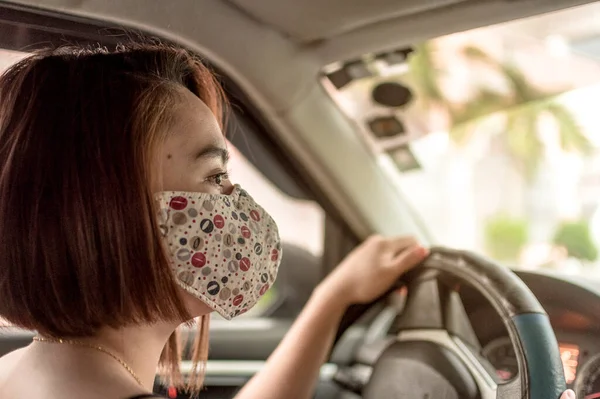 フェイスマスクをしたアジア系女性がハンドルでターン 小さな車の中で — ストック写真