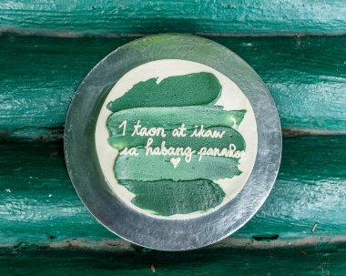 Yeşil kremalı küçük minimalist bir pastanın üst görüntüsü. Tagalog kelimeleri 1 yıl ve sonsuza kadar tercüme edilir. Yıldönümü pastası. Filipin tatlısı.