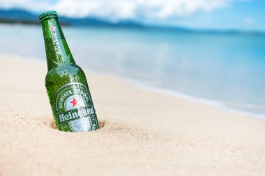 Bir şişe Heineken birası kısmen tropik bir sahil kenarındaki kuma gömülebilir..