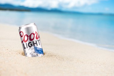 Bir kutu Coors Light Birası kısmen tropikal bir plajda kumda gömülü..