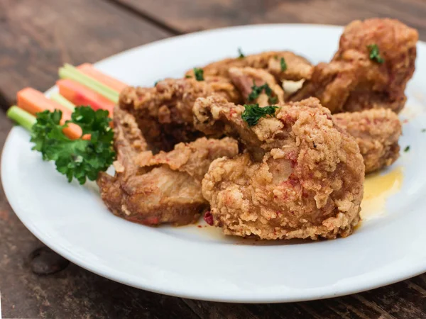Dışarıdaki ahşap bir masada beyaz bir tabakta süslenmiş bufalo kanatları..
