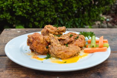 Kırsal bir bahçe restoranında beyaz bir tabakta havuç ve kereviz çubuklarıyla bufalo kanatlarının yakın çekimi..