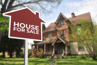 Eski tarz bir evin önünde satılık tabelası şeklinde kırmızı bir ev. Emlak kavramı.