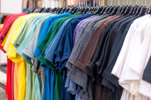 A selection of t shirts of a various colors displayed on a clothes rack at a department store.