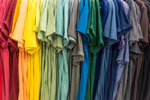 A selection of t shirts of a various colors displayed on a clothes rack at a department store.