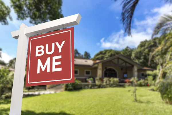 A yard sign with the words Buy Me in front of a bungalow style house. Real estate concept.