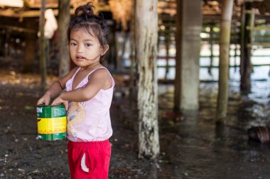 Buri Adası, Catbalogan, Samar, Filipinler - Jan 2016: Küçük bir kız, sahilin yakınlarındaki yükseltilmiş bir evin cambaz ayaklıklarının yanında kullanılmış boya kutusuyla oynuyor