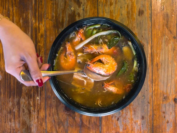 A hand scoops a shrimp from Sinigang soup with a spoon. Sinigang na Hipon Soup is a popular Filipino dish.