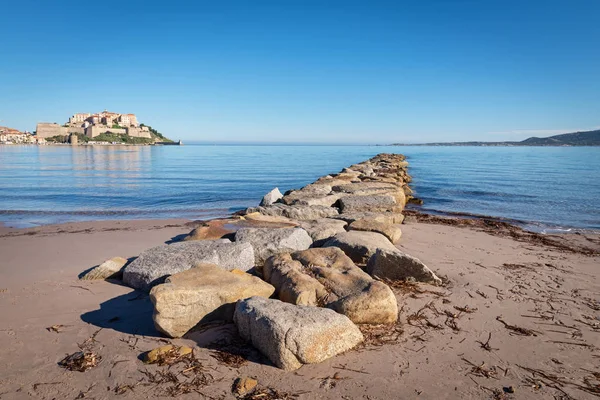 Vlnolam od velkých přírodních kamenů na pozadí Citadela města Calvi — Stock fotografie