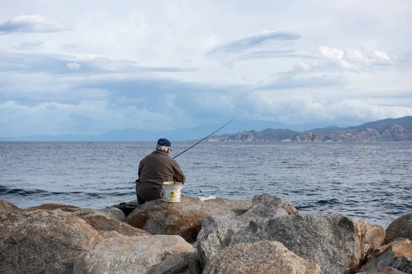 L'ILE-ROUSSE, HAUTE- CORSE/FRANCE - OCTOBER 31, 2018: A man is  fishing on the rocky shore of the Mediterranean Sea — Stock Photo, Image