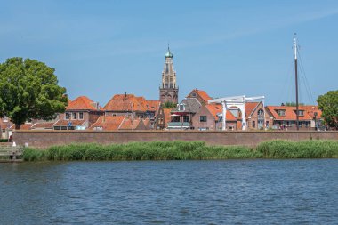 ENKHUIZEN; NORTH HOLLLAND / NETHERLANDS - 23 Haziran 2020: Güneşli bir yaz gününde IJsselmeer 'den bir kilise kulesi ile eski kasabanın görüntüsü