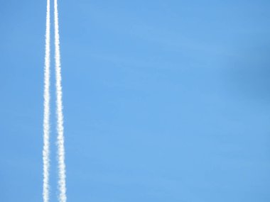 Uçak açık mavi gökyüzünde uçuyor ve ona karşı iz sürüyor, motorun egzozu arkamızda oluşmaya başlıyor, mavi gökyüzü ve bulutlar üzerinde jet kontrastları veya patikaları oluşuyor..