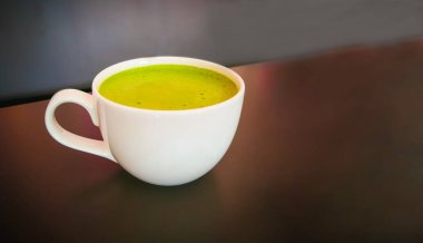 Beyaz bardakta sıcak yeşil çay, ahşap bir masada fotokopi ile birlikte..