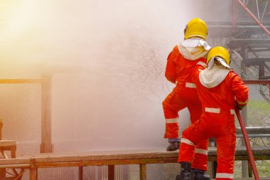 Yangın söndürücü ve hortumla yangın söndürücü kullanan iki cesur itfaiyeci ateş etmek için yüksek basınçlı su sıkan itfaiyeci tehlikeli alevlerle eğitimli itfaiyeci uzay görüntüsünü kopyalayın.