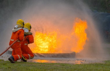 Yangın söndürücü ve hortumla yangın söndürücü kullanan iki cesur itfaiyeci ateş etmek için yüksek basınçlı su sıkan itfaiyeci tehlikeli alevlerle eğitimli itfaiyeci uzay görüntüsünü kopyalayın.