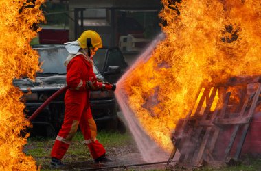 Yangın söndürücü ve hortumla yangın söndürücü kullanan cesur itfaiyeciler yangın söndürmek için yüksek basınçlı su sıkarken itfaiyeciler tehlikeli alev görüntüsü ile itfaiyecileri eğitiyorlar.