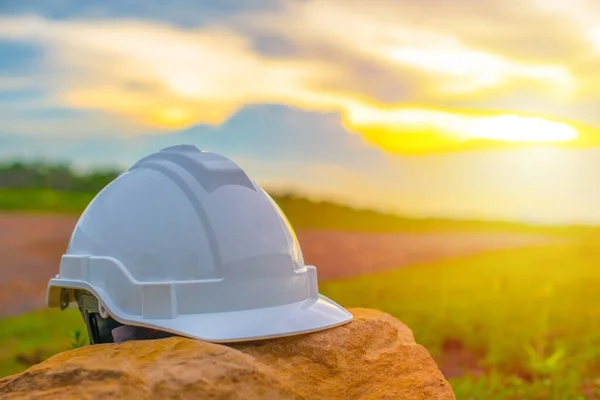 Close up of white safety helmet placed on the stone with sunset and blue sky background, Helmet in construction site after work during the sunset, Safety and Engineering Concept.
