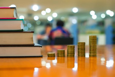 Gelir grafiği gibi altın para yığınları, farklı pozisyonlarda beş para yığını, Tayland para birimi ve bokeh arka planlı kitaplar, yatırım ve iş dünyasındaki büyüme kavramı.