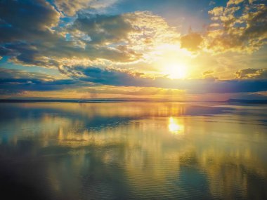 Gökyüzünde güzel bir gün batımı, gökyüzünde mavi ve turuncu güneş ışığı, gökyüzündeki bulutlar, turuncu ve denizin üzerindeki kırmızı dramatik renkler.