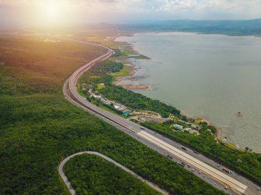 Resimli asfalt yol, dağlarla ve ormanlarla, dağlardan aşağı kıvrılan bulutlarla ve mavi gökyüzü arkaplanıyla birlikte çevreyi dolaşmaktadır. Yerel ulaşım kavramı.