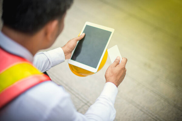 Мужчина-инженер держит планшет и кредитки с желтым шлемом.