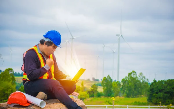 Engineer sitting with laptop, Very happy and excited man doing winner gesture with arms raised, Smile expressing winning engineer with wind turbine background, Successful and Celebration concept.