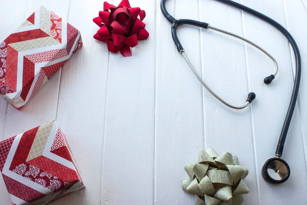 Gifts in red and white wrapping paper, bows and phonendoscope on white wooden table