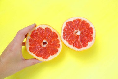 Sarı arka planda iki sulu kırmızı greyfurt, sağlıklı beslenme, gençlik ve güzellik kavramı.