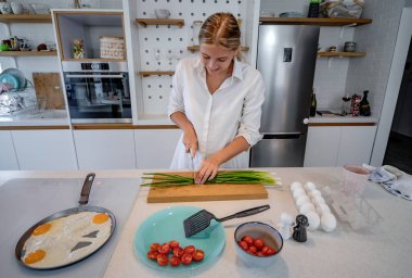 Modern donanımlı bir mutfakta yemek pişiren güzel genç bir kadın. Kızarmış yumurtaları hazırlıyorum. Evde yalnız kahvaltı..
