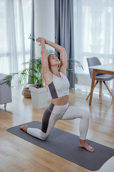  Güzel aktif genç kadın yoga yapıyor. Virabhadrasana Savaşçısı 1 evde poz veriyor. Sağlıklı yaşam tarzı ve spor anlayışı. Bir dizi egzersiz pozu.