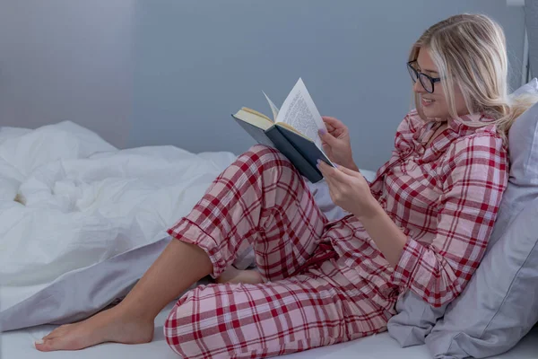 穿着睡衣的年轻漂亮的女人在家里躺在床上看书 生活方式和休闲概念 — 图库照片