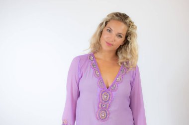 Lila Kaftanlı güzel sarışın kadın beyaz arka planda gülümsüyor.