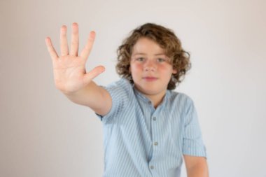 Mavi gömlekli çocuk dur işareti yapıyor.