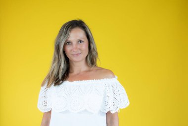 Beyaz gömlekli güzel bir kadın sarı arka planda gülümsüyor.